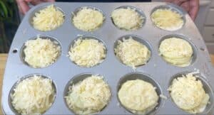 Muffin tin filled with shredded cheese-topped potato stacks, ready for baking.