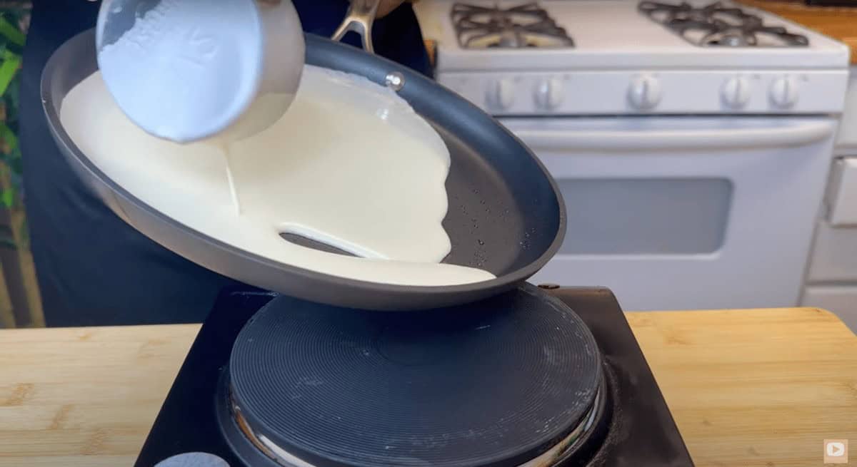 Pouring crepe batter into a hot skillet on the stove.