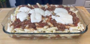 Baked ziti with creamy cheese, rich tomato sauce, and seasoned ground beef in a glass casserole dish.