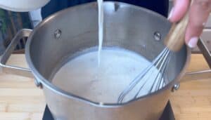 Whisking creamy sauce in a stainless steel pot on a stovetop, highlighting a cooking process step.