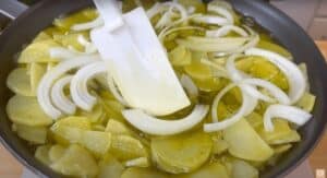 Sliced potatoes and onions cooking in a frying pan with olive oil, stirred with a spatula. Perfect for frying tips.