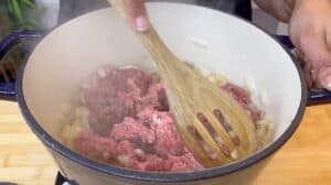 Cooking ground beef and onions in a pot, stirred with a wooden spoon. Perfect for stews or chili recipes.