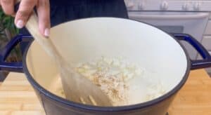 Stirring onions in a blue pot on a stove; cooking preparation in kitchen.