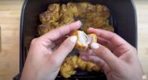 Person holding a piece of tender air fryer chicken, with more pieces in the background.