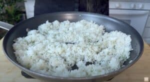 Cooking fluffy white rice with herbs in a nonstick pan, perfect for a delicious side dish.