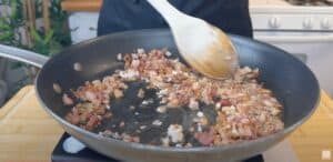 Cooking diced bacon in a skillet with a wooden spoon stirring, perfect for pasta recipes.