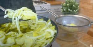 Cooking sliced potatoes and onions in oil, with a strainer in a modern kitchen setting.