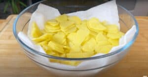 Sliced yellow potatoes in a glass bowl lined with paper towels, ready for cooking preparation.