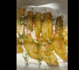 Roasted potatoes with herbs and spices on creamy yogurt in a white dish. Perfect for a flavorful vegan appetizer.