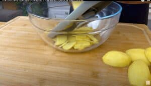 Slicing potatoes into a glass bowl on a wooden cutting board for a Spanish omelette recipe.