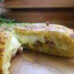 Cheesy stuffed potato omelette garnished with herbs on a wooden board, perfect for breakfast or brunch inspiration.