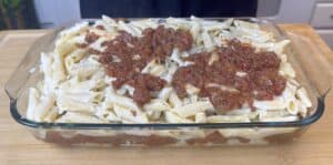 Baked penne pasta with creamy white sauce and savory meat sauce in a glass dish, ready to serve.