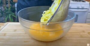 Grated potatoes being added to a bowl of beaten eggs for a cooking preparation.