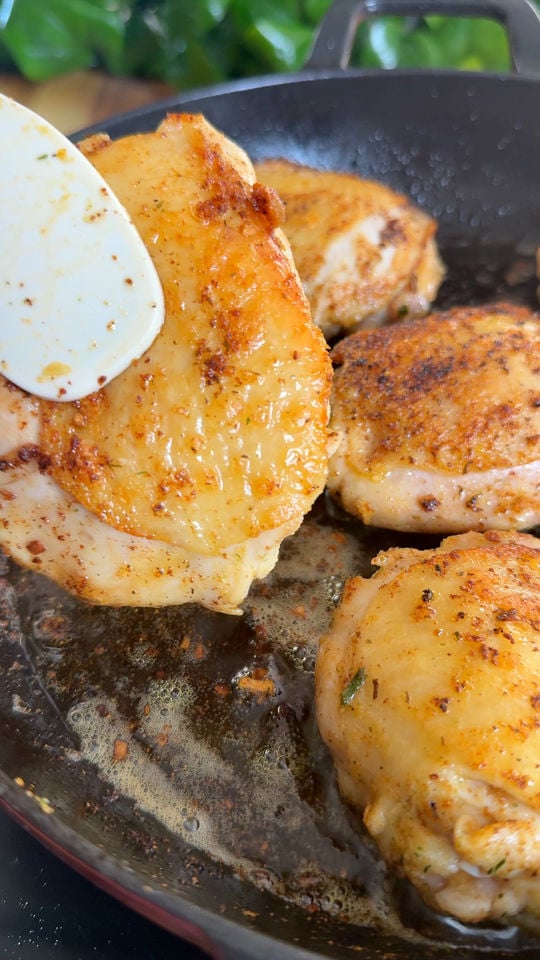 Sizzling seasoned chicken thighs cooking in a frying pan, close-up with spatula.