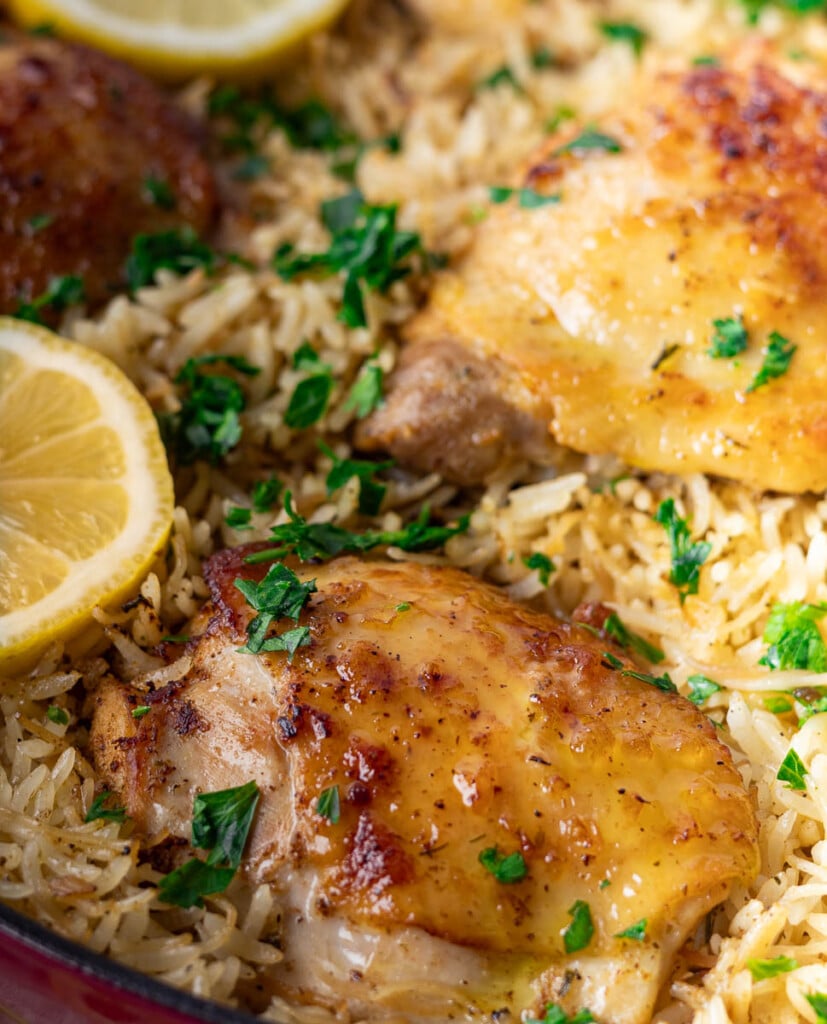 lemon garlic chicken and orzo with lemon slices, fresh parsley, and seasoned rice in a pan.