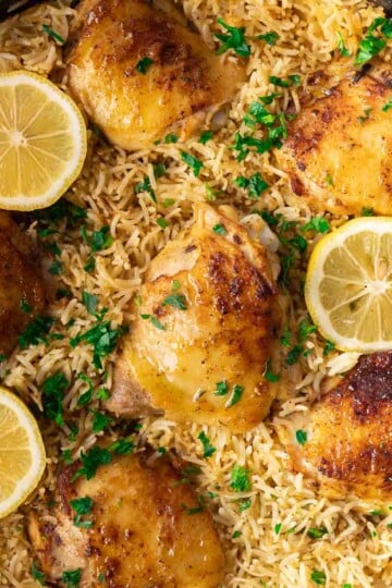Grilled chicken and rice garnished with lemon slices and parsley in a skillet.