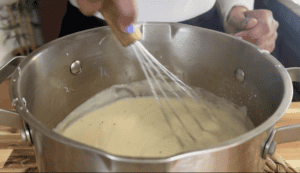 Whisking creamy sauce in a stainless steel pot for a homemade recipe.