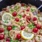 Shrimp orzo with cherry tomatoes, lemon slices, and fresh parsley in a skillet, ready to serve.