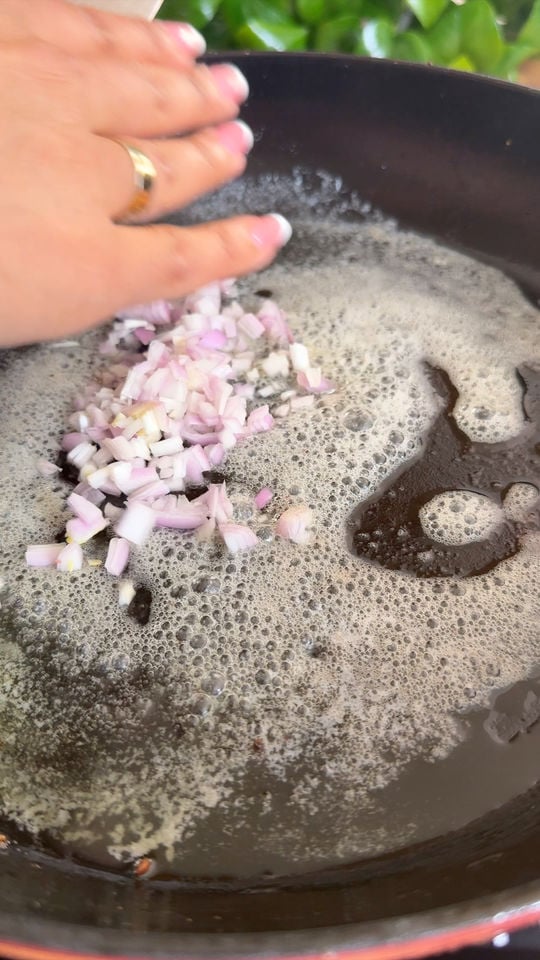 Hand adding chopped onions to sizzling butter in a frying pan.