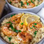 Creamy orzo pasta with seasoned shrimp, garnished with parsley and lemon slices, served in a bowl.
