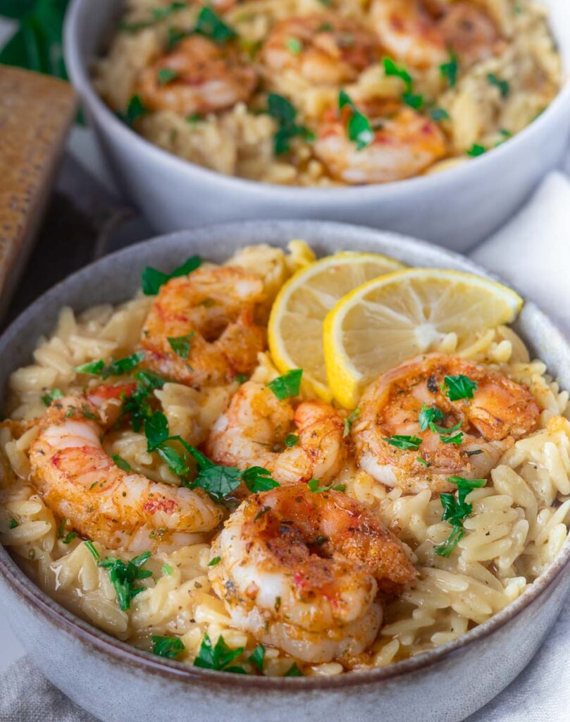 Shrimp scampi orzo with seasoned shrimp, garnished with parsley and lemon slices, served in a bowl.