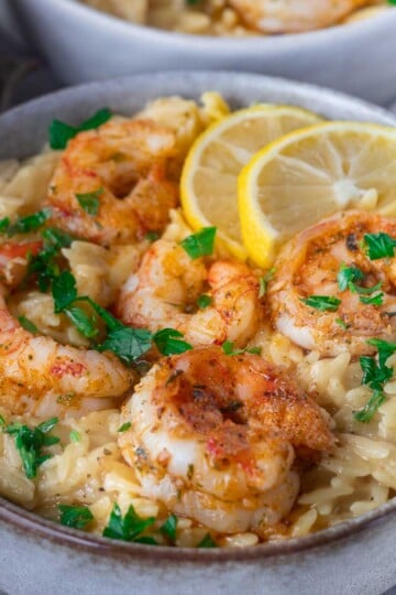 Bowl of orzo with seasoned shrimp, garnished with lemon slices and parsley.