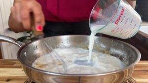 Pouring milk into a skillet while whisking for a creamy sauce preparation.