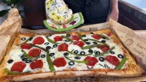 Freshly baked rectangular pizza with pepperoni, olives, and green peppers on parchment paper.