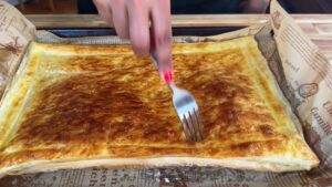 Golden flaky puff pastry being pierced with a fork on a baking tray.