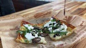 Savory mushroom pastry topped with goat cheese, fresh herbs, and balsamic glaze on a rustic wooden table.