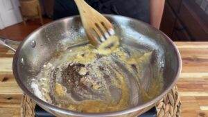 Cooking roux in a pan with wooden spoon, preparing base for sauces or soups on wooden countertop.