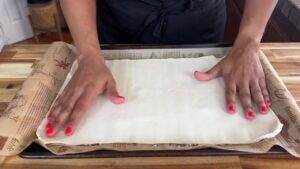 Hands preparing dough on a baking tray lined with parchment paper, ready for baking.