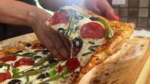 Hand grabbing a cheesy pepperoni pizza slice with olives and green peppers.