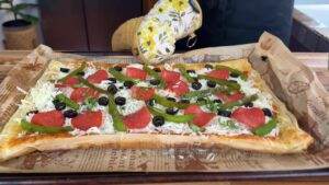 Freshly baked rectangular pizza with pepperoni, green peppers, black olives, and cheese on parchment paper.