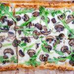 Sliced mushroom and arugula pizza on crispy crust with melted cheese.