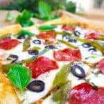 Delicious homemade pizza with pepperoni, olives, green peppers, and basil leaves on a wooden board.