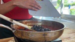 Cooking black olives in tomato sauce with wooden spoon in a pan, kitchen scene.