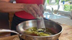 Grating fresh garlic into olive oil in a pan, enhancing flavor for a delicious dish. Cooking preparation in action.