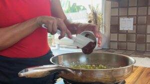 Person cooking in kitchen, adding ingredient to sautéing onions in stainless steel pan, close-up shot.