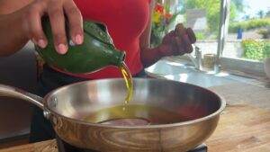 Pouring olive oil into a frying pan on a sunny kitchen counter.