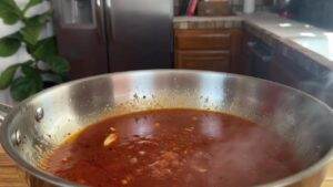 A simmering pot of homemade tomato sauce with garlic and spices in a stainless steel pan, kitchen backdrop.