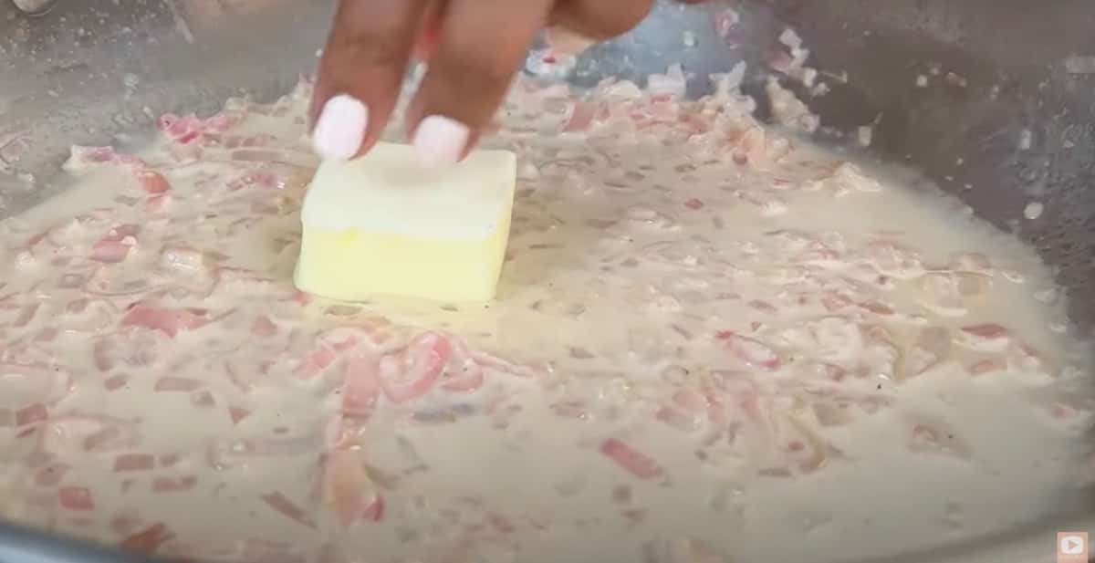 Adding butter to creamy onion sauce in a pan, enhancing flavor and texture.