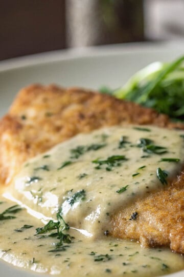 Lemon beurre blanc chicken on a white plate with dill.