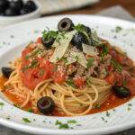 Plate of spaghetti with tomato sauce, olives, and cheese, garnished with parsley.