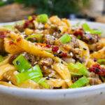 Spicy stir-fried noodles with beef, green onions, and sesame seeds in a white bowl, served on a wooden table.