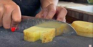 Close-up of hands slicing a peeled potato into cubes with a knife on a cutting board.