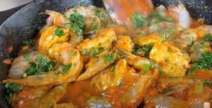 Sizzling shrimp in a spicy tomato sauce with fresh herbs in a pan, creating a flavorful seafood dish.