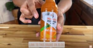 Person holding Nando's Medium Peri-Peri sauce bottle on a wooden table. Gluten-free and non-GMO.