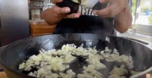 Chopped onions sautéing in a cast iron skillet on a kitchen stove.