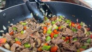 Sizzling beef stir-fry with bell peppers, mushrooms, and onions in a pan, being tossed with tongs.